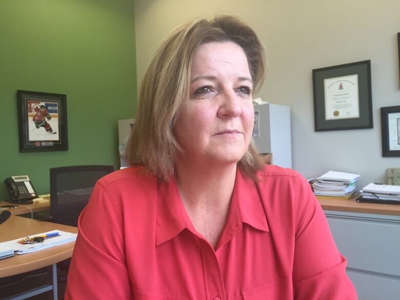 A person in an a pink shirt seated at a desk in an office looking off into the distance.