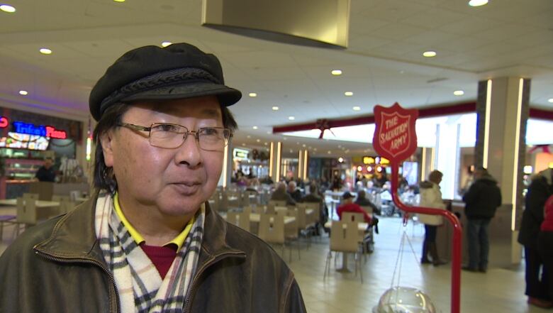 a man in a dark jacket and hat stands in a food court