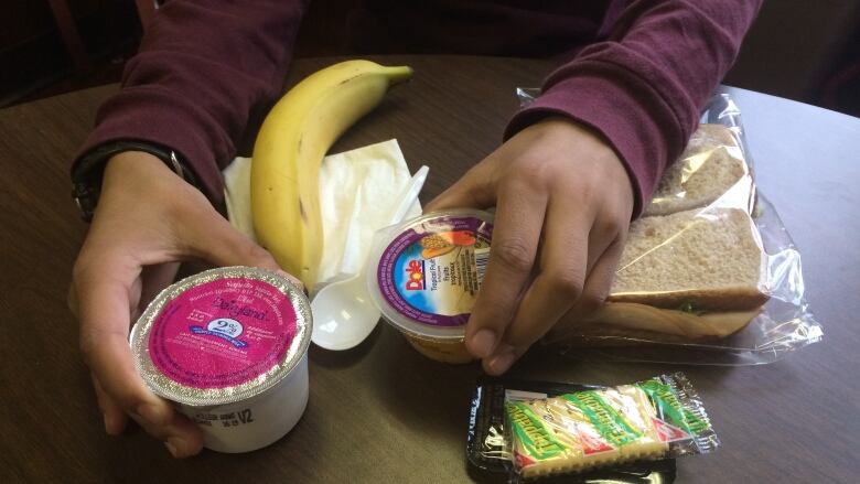 A close up of a school meal with a banana, sandwich, crackers and containers of yogurt and fruit.