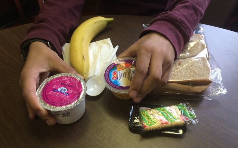 A close up of a school meal with a banana, sandwich, crackers and containers of yogurt and fruit.