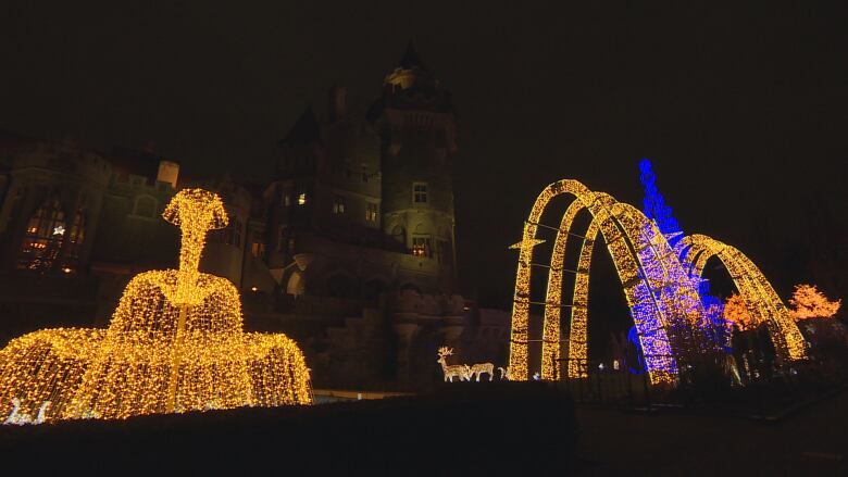 A dark castle at night with Christmas lights on outdoor trees in the foreground.