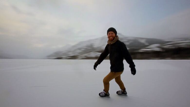 A man skates on a frozen lake, smiling. 