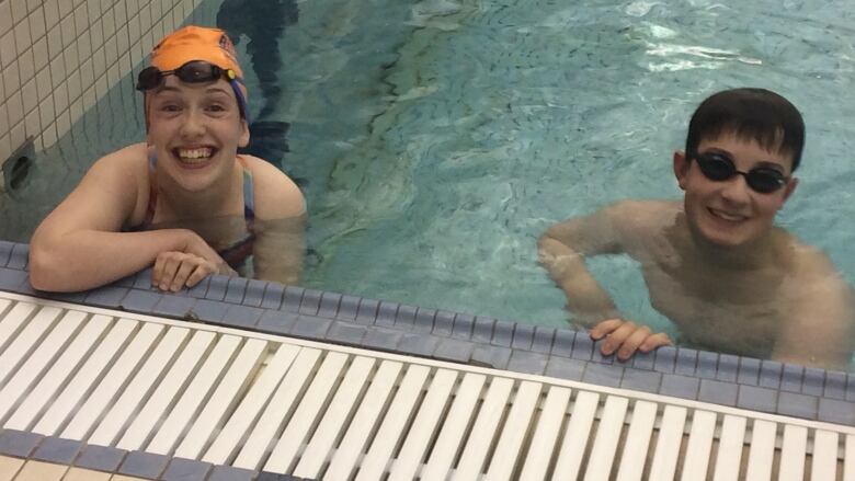 Two young swimmers with googles on smile at the camera 