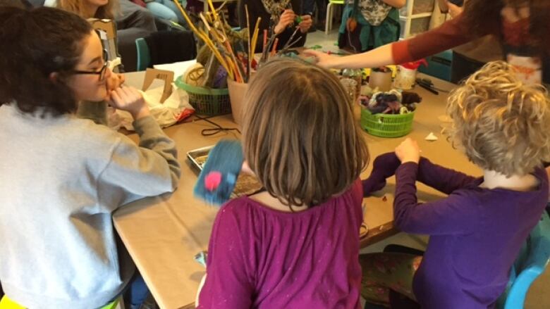 Children with their backs to the camera use various art supplies on a table