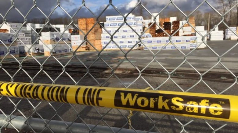 A yellow line with the words 'Investigation Line WorkSafe' is seen behind a steel wire fence, with pallets visible in the background.