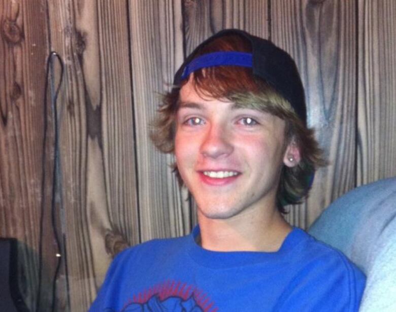 A young male with medium length hair under a baseball cap poses for a picture.