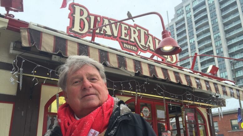 A man in a scarf poses next to a food stand.