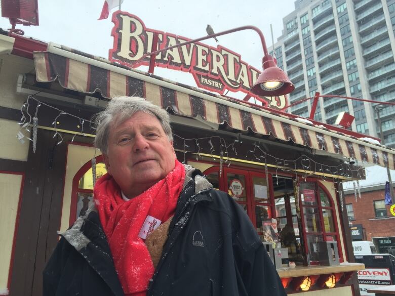 A man in a scarf poses next to a food stand.