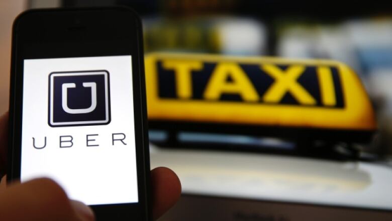 An Uber logo on a smartphone next to a taxi sign on top of a cab.