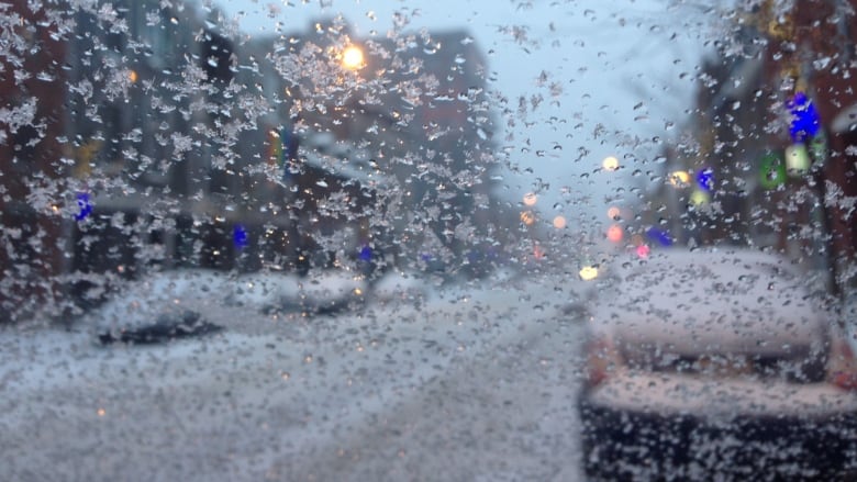 A window with ice pellets looks out onto a street.