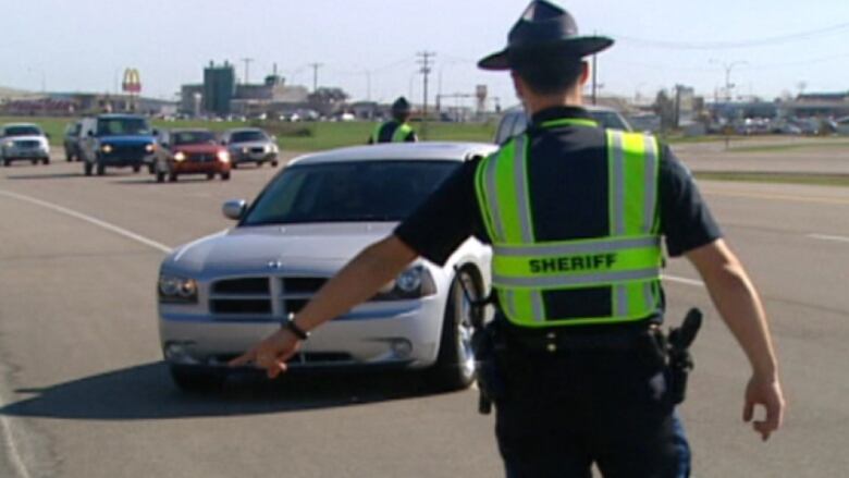 A person wearing a sheriff's jacket directs a car to pull to the side of the road.