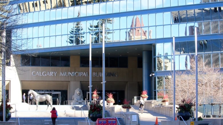 Sun shines on the steps leading to the doors of a large, blue glass building.