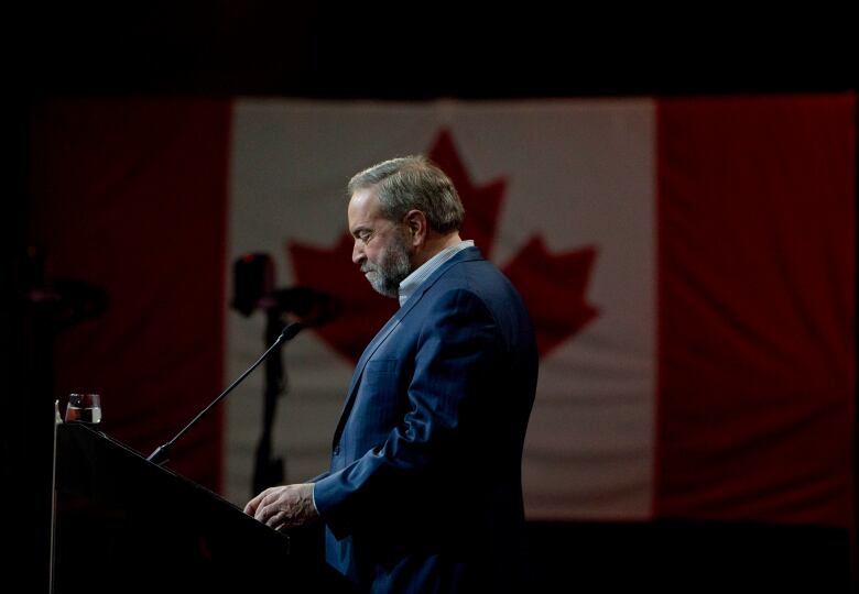 A bearded man stands in profile in front of a Canadian flag.