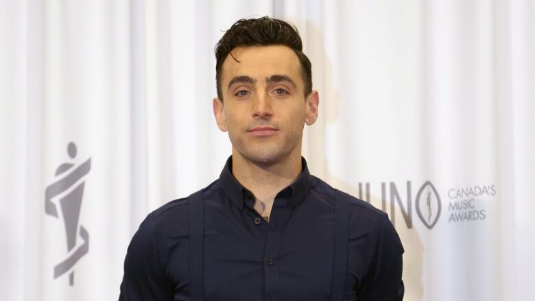 A person stands in front of a backdrop decorated with the Juno awards logo.