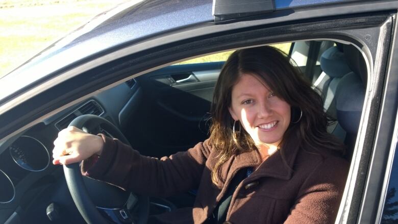 A smiling woman sits behind the wheel of a car. 