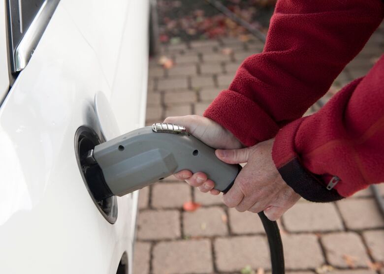 Two hands can be seen putting an electric charger into the side of a white car.