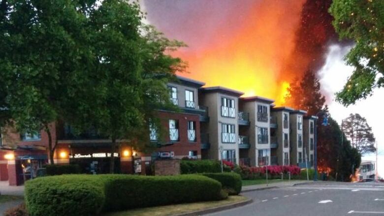 Red flames shooting from the roof of an apartment complex light up the night sky.