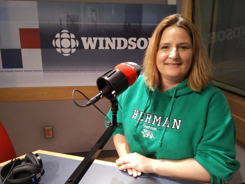 A woman wearing a green hoodie sitting in front of a mic in a radio studio