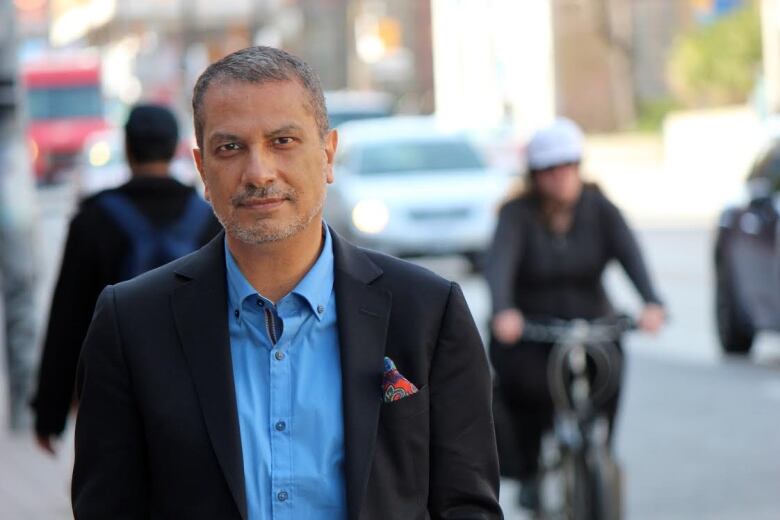 A man in suit stands near a traffic road.