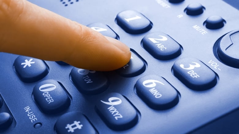 A close up image shows a finger pressing a number on a phone.