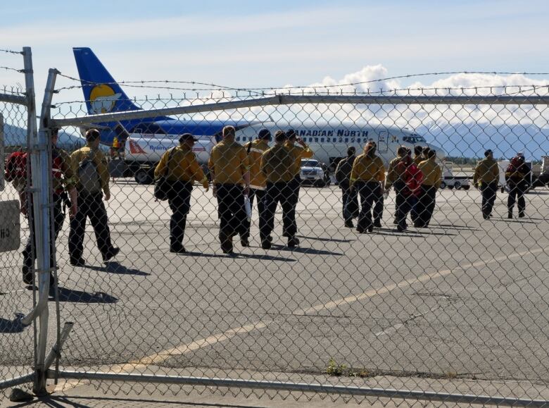 A line of people are seen walking behind a fence toward an airplane on the tarmac.