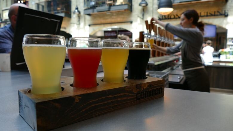 picture of a flight of beers as a woman pours beer in the background