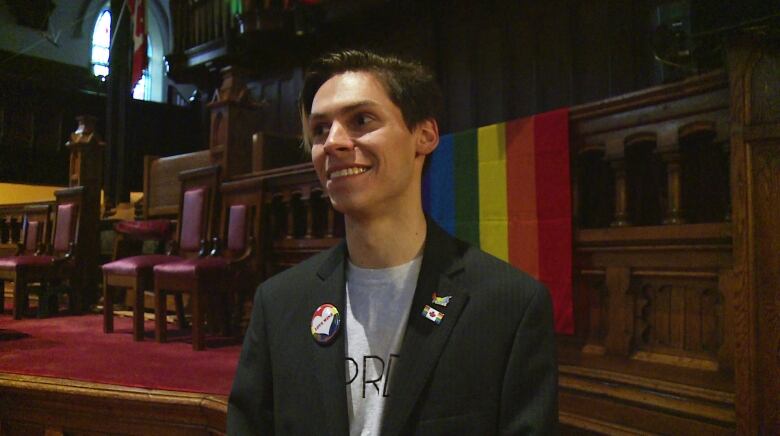 Tyler Murnaghan in church with Pride flag in background.