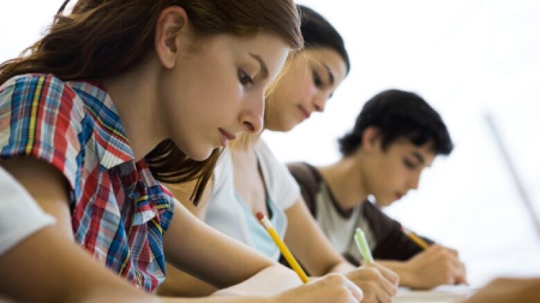 A close up of students writing exams at desks 