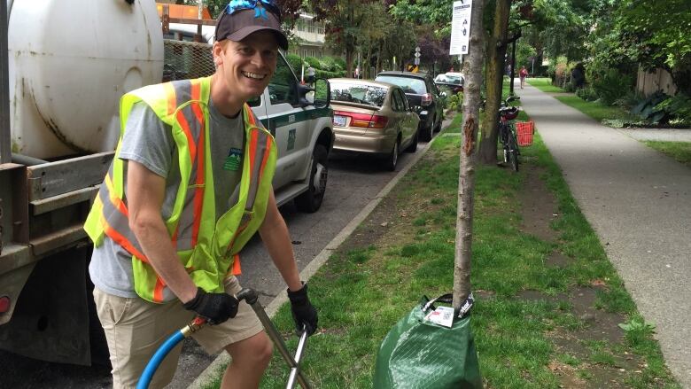 A city tree waterer uses a steel watering probe to deliver hydration deep into the ground, closer to this tree's root bulb and also to fill the tree bag wrapped around its base.