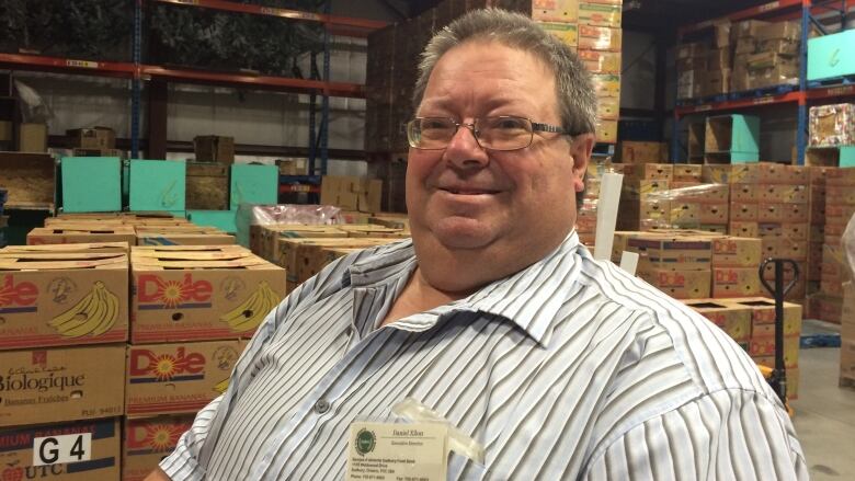 A man with glasses in a warehouse full of boxes.