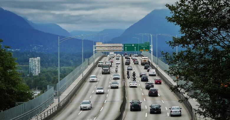 Rows of cars and bikes cross a bridge leading into the mountains.