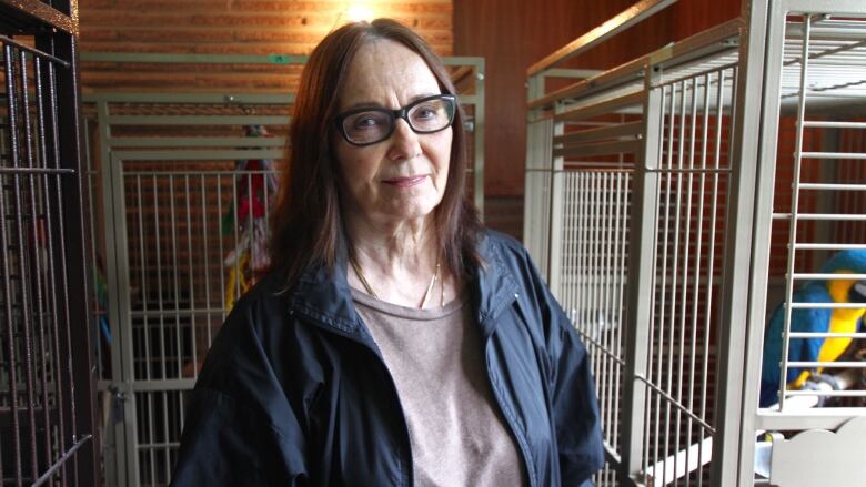 A woman with shoulder-length brown hair, black-framed glasses and wearing a dark blue coat looks into the camera.