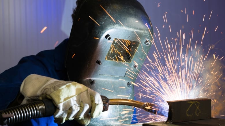 A welder is shown in a mask while holding a welding rod as sparks fly.