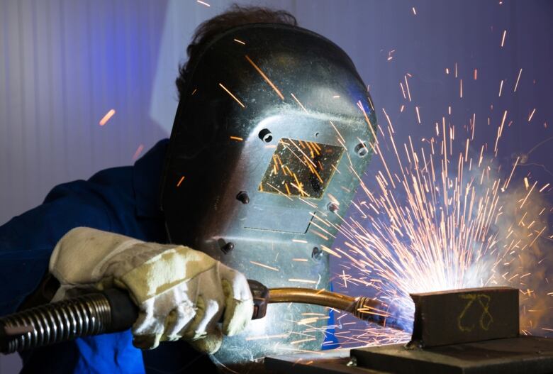 A welder is shown in a mask while holding a welding rod as sparks fly.