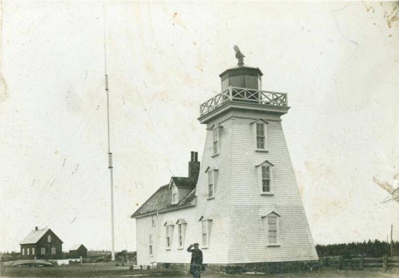 A black and white view of a lighthouse with a large antennae behind it