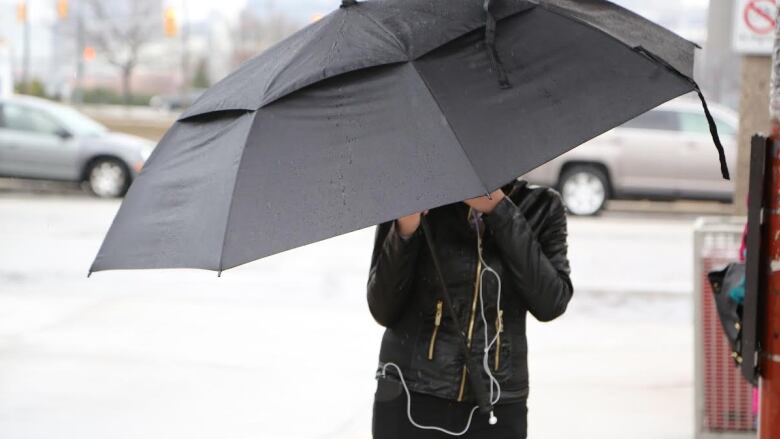 A person covering from the rain with an umbrella, the umbrella is also covering their face.