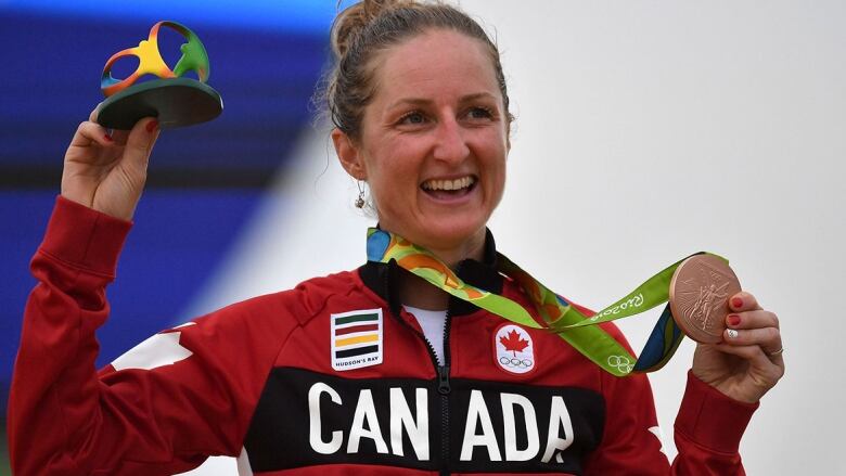 A woman in a Canada zip-up sweater celebrates with a bronze medal