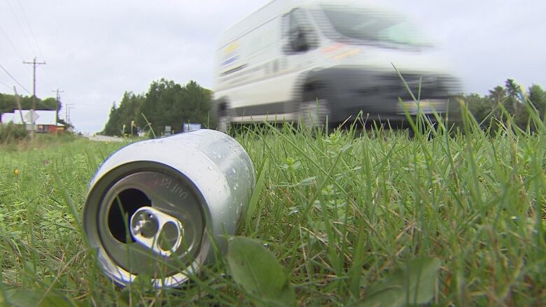 A can on the side of the road as a vehicle whizzes by.