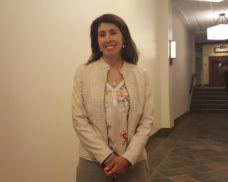 A woman with brown hair wearing a floral shirt and a white blazer poses for a photo. 