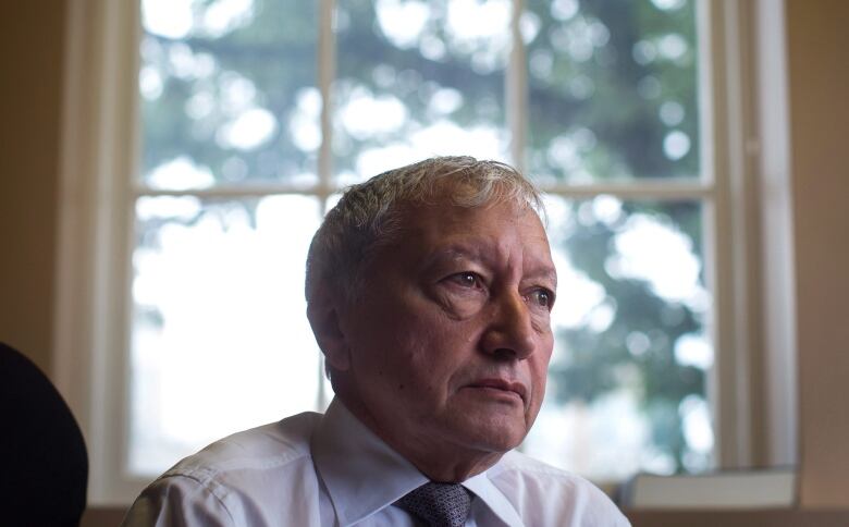 A man looks off into a distance, while seated in front of a window.