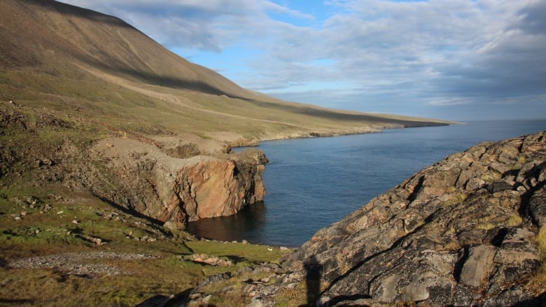 Two rocky pieces of land are cut by the blue ocean and a blue sky with clouds in the weekend. 