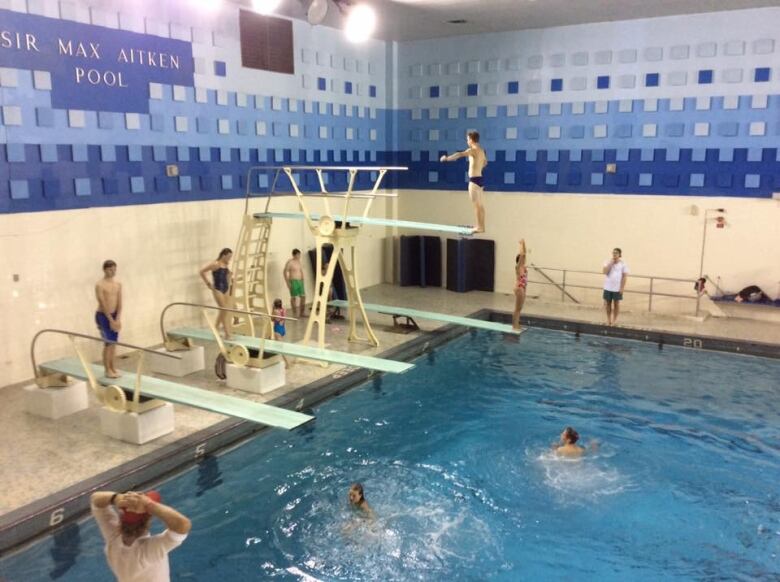 A pool with four diving boards and people swimming