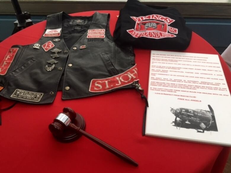 A leather vest and other items arranged on a red tablecloth.