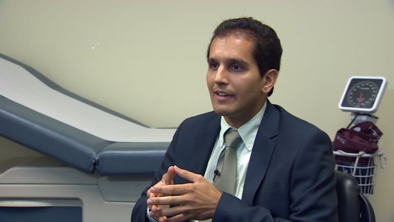 A docor sits in a suit in an exam room 