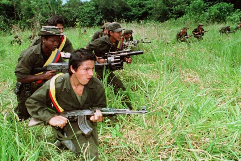 Roughly a dozen soldiers, brandishing assault rifles and grenade launchers, move through tall grass.