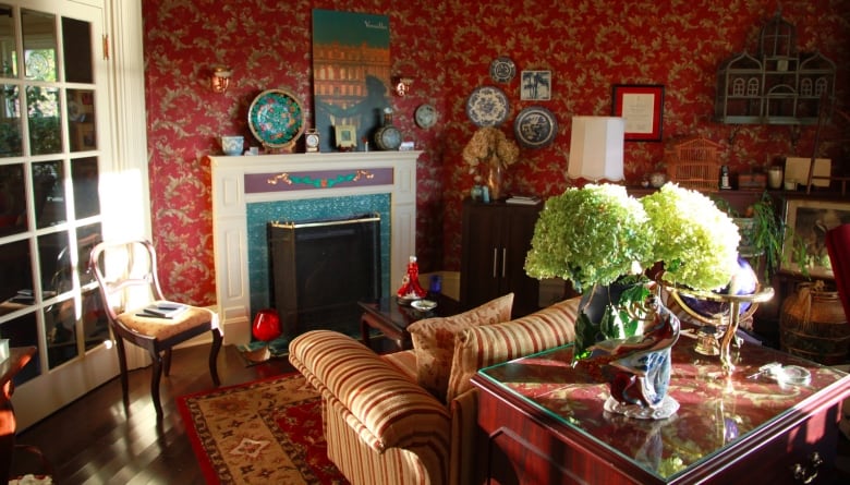 A living room with red-patterned wallpaper and a fireplace. On a wooden table there are fresh flowers.