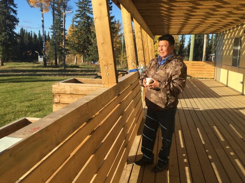 A man stands squint in the sun on a wooden deck. He is warming a camo jacket.