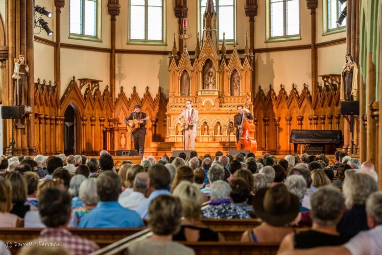 Three musicians perform while a large crowd listens at historic St. Mary's Church as part of the Under the Spire music festival. 