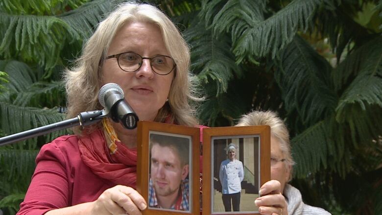 A woman holds a photo of a young man while speaking into a microphone.