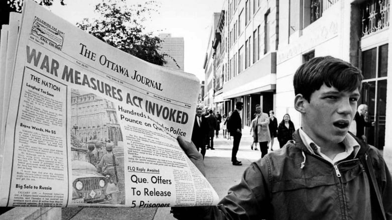 A newsboy in Ottawa holds up a newspaper